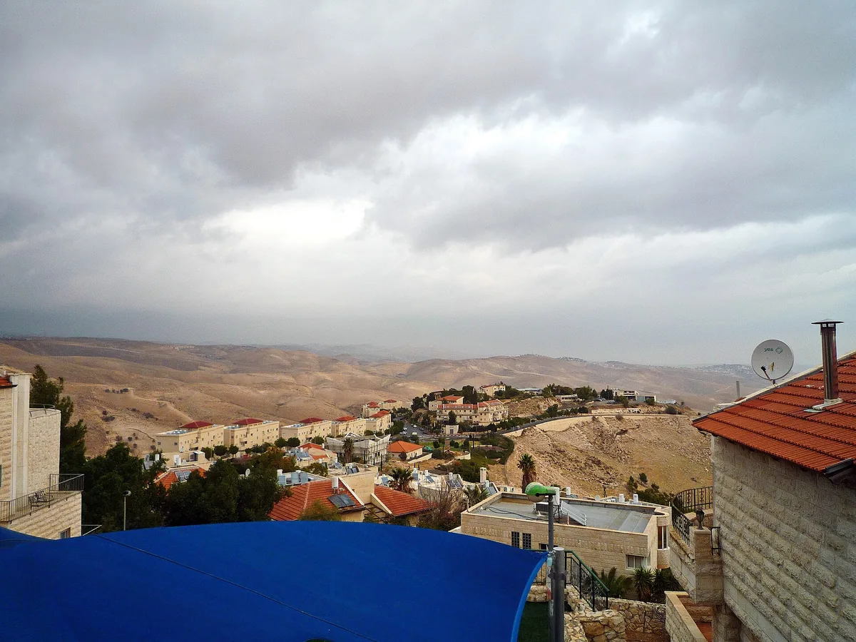 Homes in Mitzpe Nevo under a cloudy sky, with desert hills beyond, seen from Klei Shir